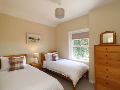 A bedroom with two single beds a bedside table with lamp a chest of drawers and a window at 2 Twizel Station Cottage Cornhill-on-Tweed near Norham
