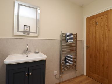 A bathroom with a sink cabinet mirror heated towel rail with towels and a wooden door at 2 Twizel Station Cottage Cornhill-on-Tweed near Norham