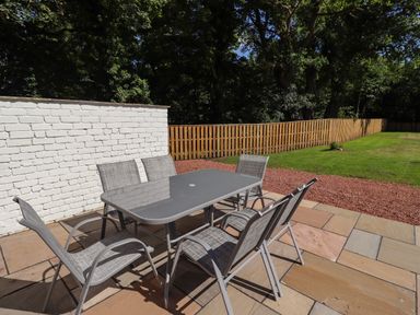 An outdoor patio with a glass table and six chairs next to a white brick wall and wooden fence at 2 Twizel Station Cottage Cornhill-on-Tweed near Norham
