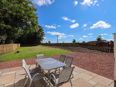An outdoor patio area with a glass table and six chairs overlooking a grassy yard with a wooden fence at 2 Twizel Station Cottage Cornhill-on-Tweed near Norham