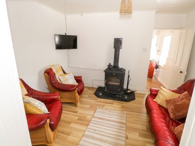 A living room with red leather sofas a wood stove TV on wall and a rug on wooden floor at Marys Cottage Theur near Riverstown County Sligo