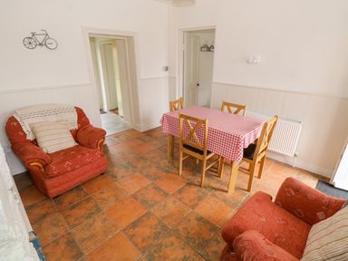 A dining room with a table covered in a red and white checkered tablecloth and four wooden chairs with two red upholstered armchairs at Marys Cottage Theur near Riverstown County Sligo