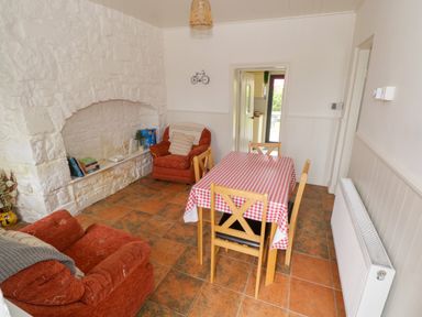 A dining room with a table covered with a red and white checkered tablecloth and four chairs two armchairs and a white stone fireplace at Marys Cottage Theur near Riverstown County Sligo