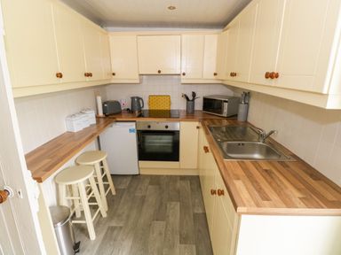 A kitchen with wooden countertops stools a sink oven microwave kettle and cabinets at Marys Cottage Theur near Riverstown County Sligo