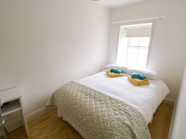 A bedroom with a bed, folded towels on the bed, a window with a blind, and a small white table at Marys Cottage in Theur near Riverstown, County Sligo