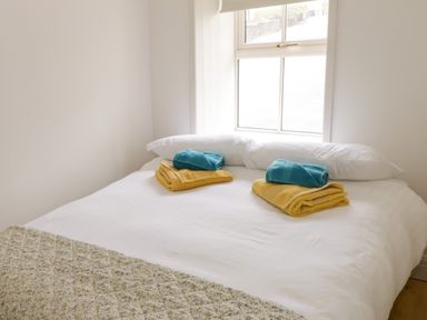 A bed with white pillows and folded yellow and blue towels on top near a window at Marys Cottage Theur near Riverstown County Sligo