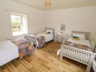 A bedroom with three single beds and a small desk with a chair at Marys Cottage Theur near Riverstown County Sligo