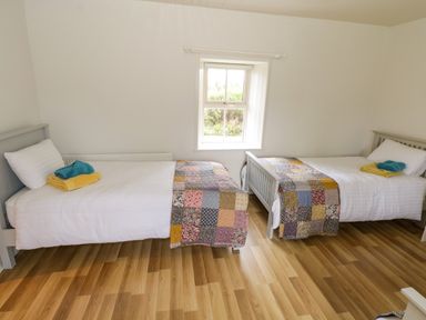 A bedroom with two single beds with white bedding and patchwork quilts under a window at Marys Cottage Theur near Riverstown County Sligo