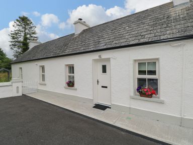 Exterior front view of a white single-story cottage with three windows flower boxes and a door at Marys Cottage Theur near Riverstown County Sligo