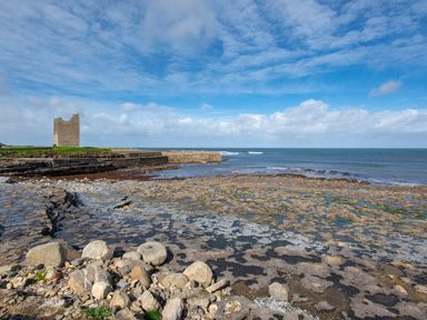 A rocky coastline with a stone tower and a sea wall under a blue sky at Marys Cottage in Theur near Riverstown County Sligo