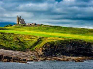 A castle and buildings on a green hill by the rocky coastline near the sea at Marys Cottage Theur near Riverstown County Sligo