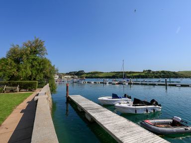 A waterfront with boats docked at a wooden pier and a grassy area with a bench at 5 Ocean Reach in Bolberry