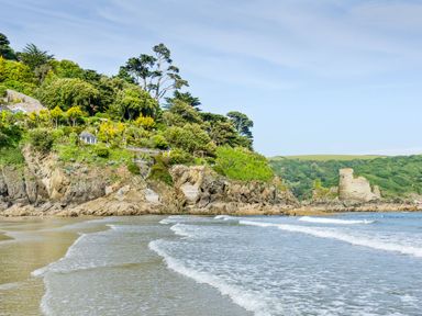 A shoreline with waves reaching a rocky cliff with trees and an old stone structure at 5 Ocean Reach in Bolberry