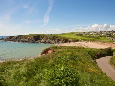 A coastal landscape with a beach rocky cliffs grassy fields and houses in the distance at 5 Ocean Reach in Bolberry