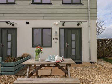 A wooden picnic table with a vase of tulips and tea set outside a house with green doors and windows at 5 Ocean Reach in Bolberry