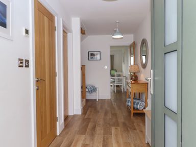 A hallway with wooden doors wooden floor a side table with a lamp a round mirror and a bench at 5 Ocean Reach in Bolberry