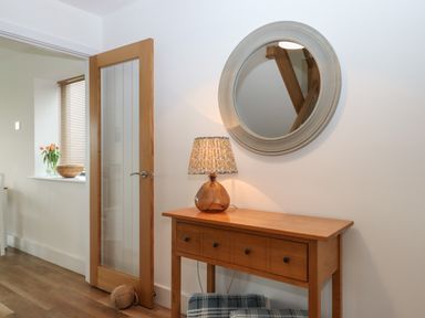 An entryway with a wooden console table a lamp a round mirror and a wooden door at 5 Ocean Reach in Bolberry