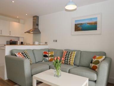 A living room with a green sofa and colorful cushions a white table with flowers and a kitchen area at 5 Ocean Reach Bolberry