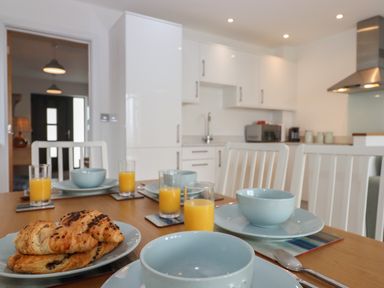 A kitchen dining area with a wooden table set with plates bowls glasses of orange juice and croissants at 5 Ocean Reach in Bolberry