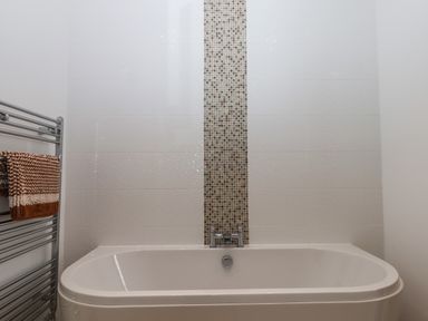 A bathtub with a tiled wall and a towel rack with a brown and white towel at 5 Ocean Reach in Bolberry