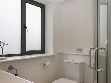 A bathroom with a frosted window a toilet a glass shower door and a small mirror on the windowsill at 5 Ocean Reach in Bolberry