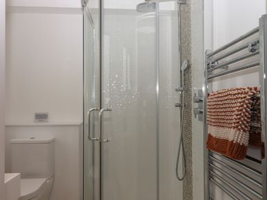 A bathroom with a toilet a glass shower enclosure a silver towel rack and a striped orange and white towel at 5 Ocean Reach in Bolberry