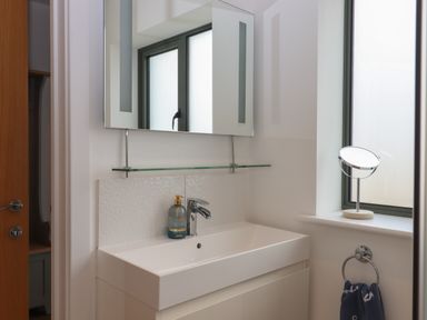 A bathroom sink with a mirror above a soap dispenser on the counter and a small round mirror on the window ledge at 5 Ocean Reach in Bolberry