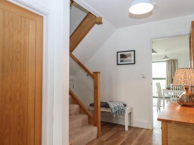 A hallway with a wooden staircase carpeted stairs and a white bench under the stairs and a wooden table with a lamp at 5 Ocean Reach in Bolberry