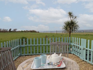 A patio table with a teapot and two cups on a tray by a blue wooden fence overlooking a grassy field and a tree at 5 Ocean Reach Bolberry
