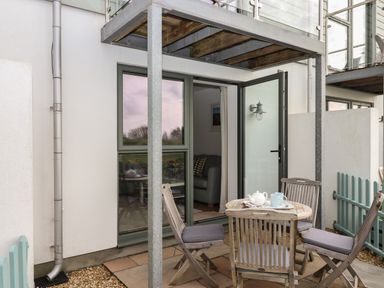 A patio with wooden chairs and table set with teapot and cup outside a building at 5 Ocean Reach Bolberry