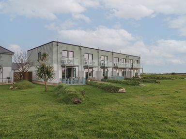 A row of modern townhouses with balconies and small fenced patios on a large grassy field at 5 Ocean Reach in Bolberry