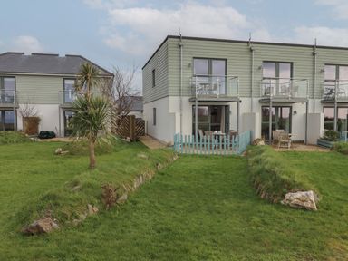 A grassy garden area with a small tree and modern two-story townhouses with balconies in the background at 5 Ocean Reach in Bolberry