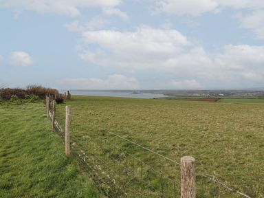 A field with grass and a wire fence with wooden posts overlooking water and distant buildings at 5 Ocean Reach in Bolberry