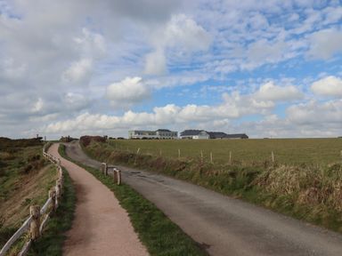 A countryside path and road with fences alongside a grassy field and buildings in the distance at 5 Ocean Reach in Bolberry