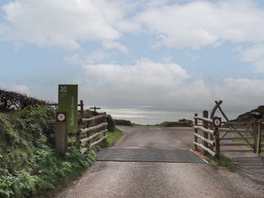 A coastal road with wooden fences and a green National Trust Bolberry Down sign at 5 Ocean Reach in Bolberry