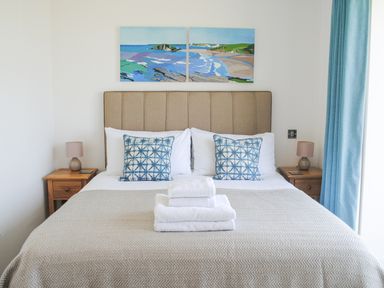 A bedroom with a bed with beige headboard two blue patterned cushions and folded white towels at 5 Ocean Reach in Bolberry