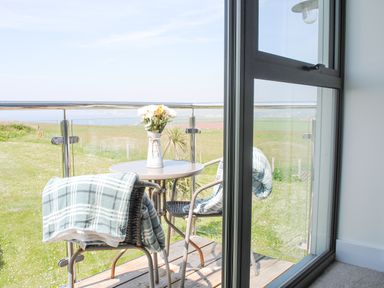 A balcony with two chairs and a round table with flowers overlooking green fields at 5 Ocean Reach in Bolberry