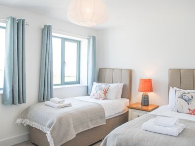A bedroom with two single beds with towels on the beds a bedside table with a lamp and blue curtains at 5 Ocean Reach in Bolberry