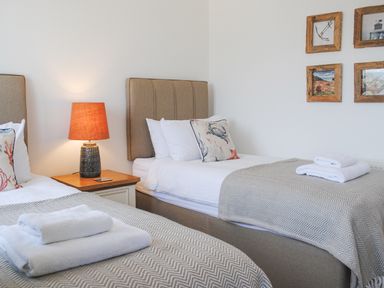 A bedroom with two single beds bedside table lamp and framed pictures on the wall at 5 Ocean Reach in Bolberry