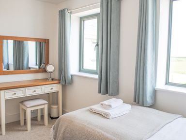 A bedroom with a bed a dressing table a stool and two windows with curtains at 5 Ocean Reach in Bolberry