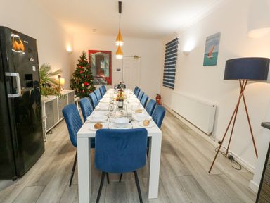 A dining room with a long white table set for a meal and blue chairs at Beachaven in Weymouth