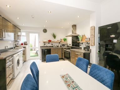A kitchen with blue chairs around a white table and wooden cabinets at Beachaven in Weymouth