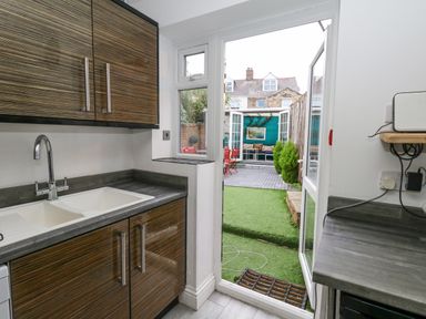A kitchen with a double sink and wooden cabinets leading to a garden with artificial grass and a seating area at Beachaven in Weymouth