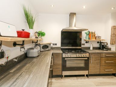 A kitchen with a stove microwave toaster and kitchen utensils on wooden shelves at Beachaven in Weymouth