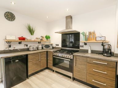 A kitchen with wooden cabinets stove and shelves with kitchen appliances at Beachaven in Weymouth