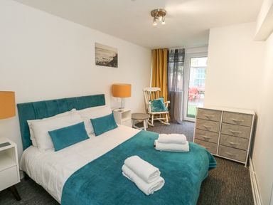 A bedroom with a bed covered in teal bedding and white towels bedside tables and lamps a rocking chair next to a window and a chest of drawers at Beachaven in Weymouth