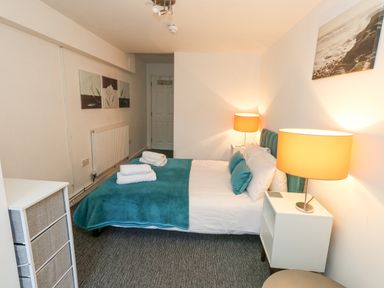 A bedroom with a double bed green blanket and pillows white bedside tables with lamps and wall art at Beachaven in Weymouth