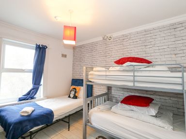 A bedroom with a single bed and a bunk bed with red pillows and blue curtains at Beachaven in Weymouth