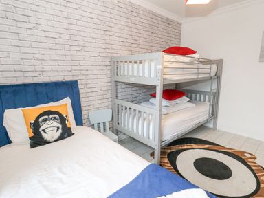 A bedroom with a single bed and bunk beds a small chair and a patterned rug at Beachaven in Weymouth