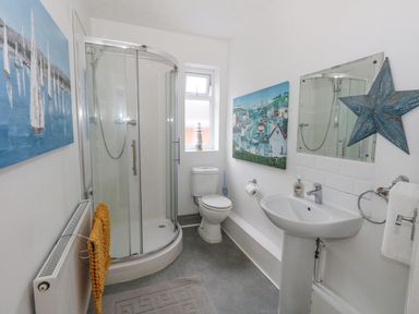 A bathroom with a corner shower, toilet, sink, towel rack, and paintings on the walls at Beachaven in Weymouth